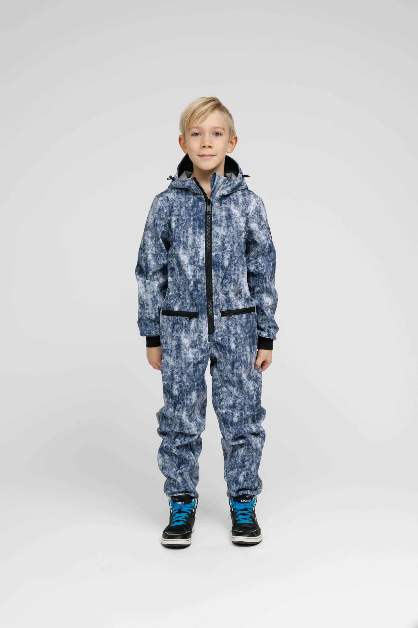 Softshell Onesie for Kids worn by a child featuring blue print, adjustable hood, and zippered pockets.
