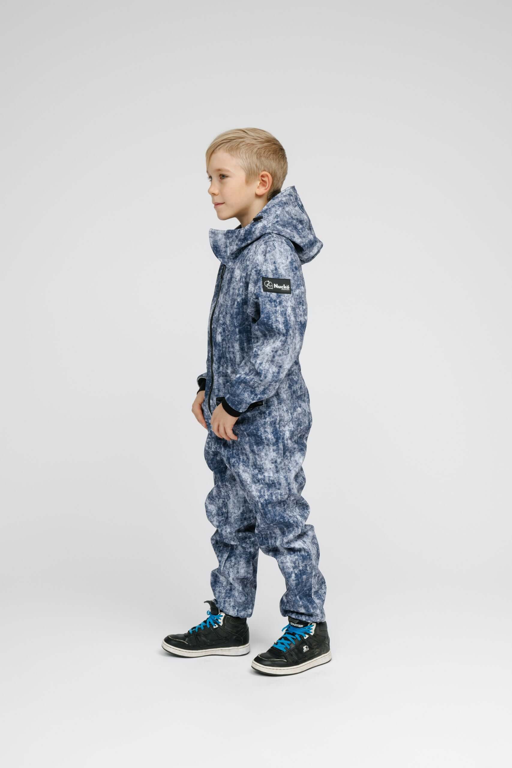 Child wearing a blue Softshell Onesie for Kids, featuring a hood and elastic cuffs, perfect for outdoor activities.