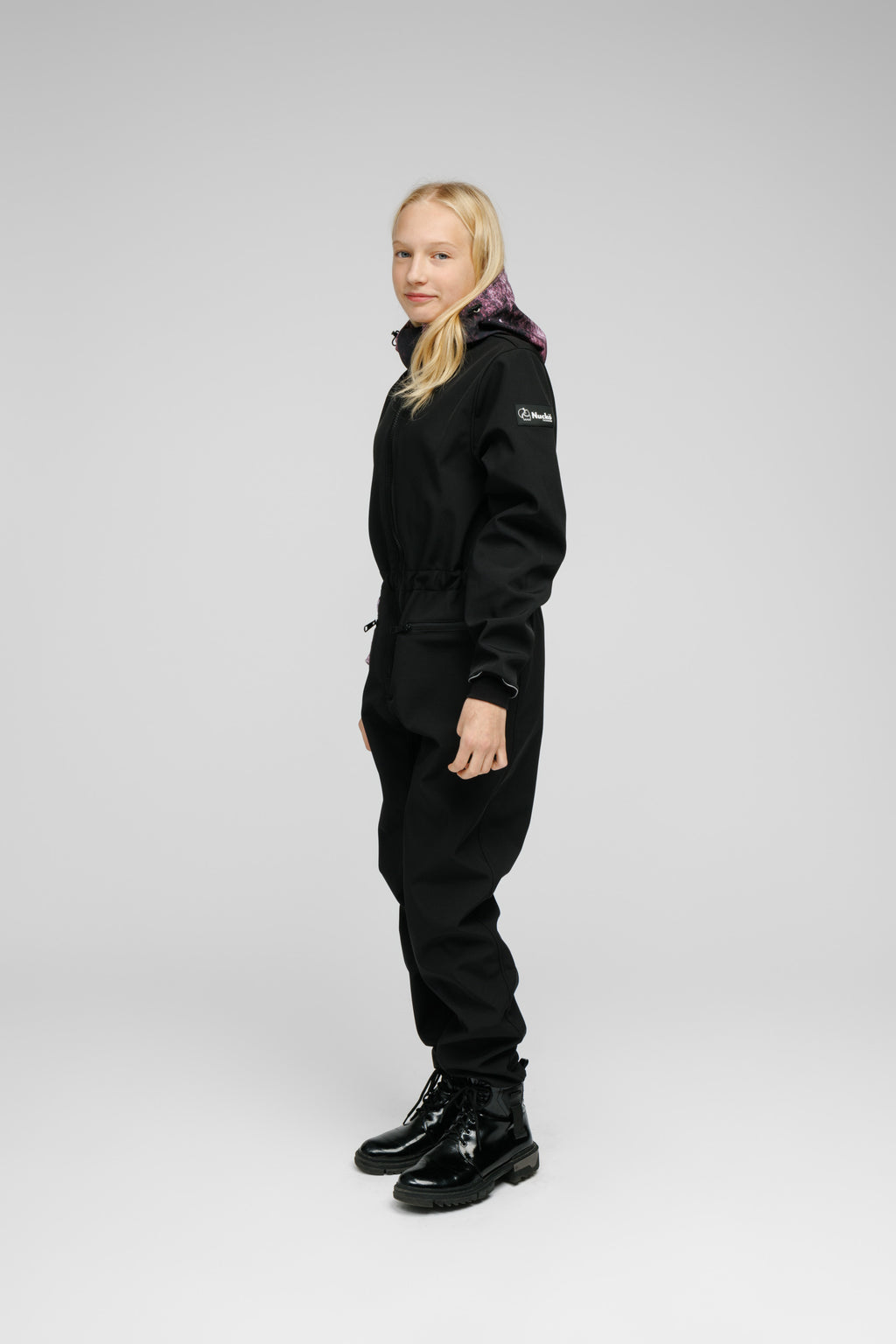 Child wearing a Softshell Onesie for Kids in black with a purple hood, showcasing adjustable features and a snug fit.