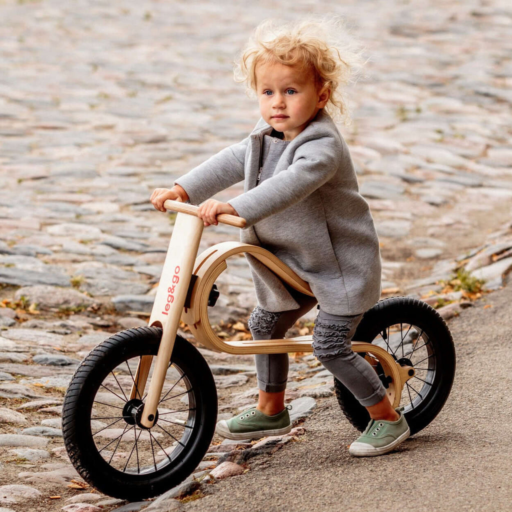 Leg&go Balance Bike 3in1 with a child riding on a cobblestone path, showcasing innovative wooden design.