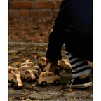 Child playing with Wooden Bus by Wooden Story and other wooden toy cars on outdoor stone surface.