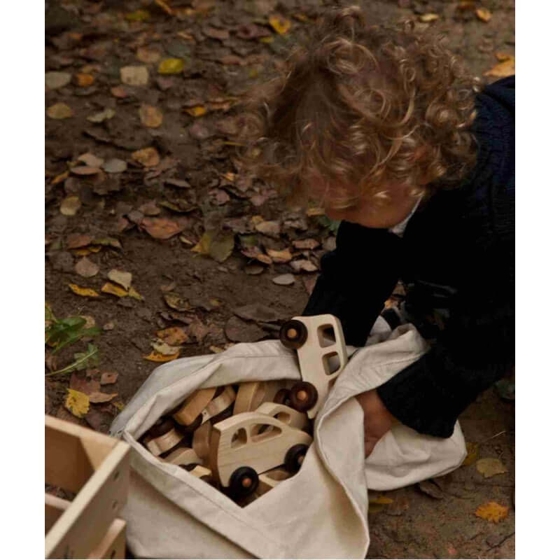 Child exploring a bag of wooden cars, including the Wooden bus by Wooden Story, surrounded by autumn leaves.