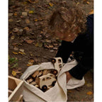 Child exploring a bag of wooden cars, including the Wooden bus by Wooden Story, surrounded by autumn leaves.