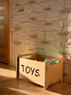 Montessori wooden toy box sitting in a stylish room, filled with colorful toys, perfect for nursery storage.