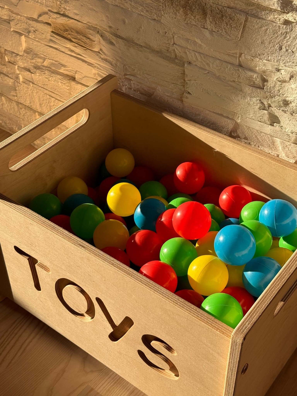 Montessori wooden toy box filled with colorful balls in a stylish nursery setting.