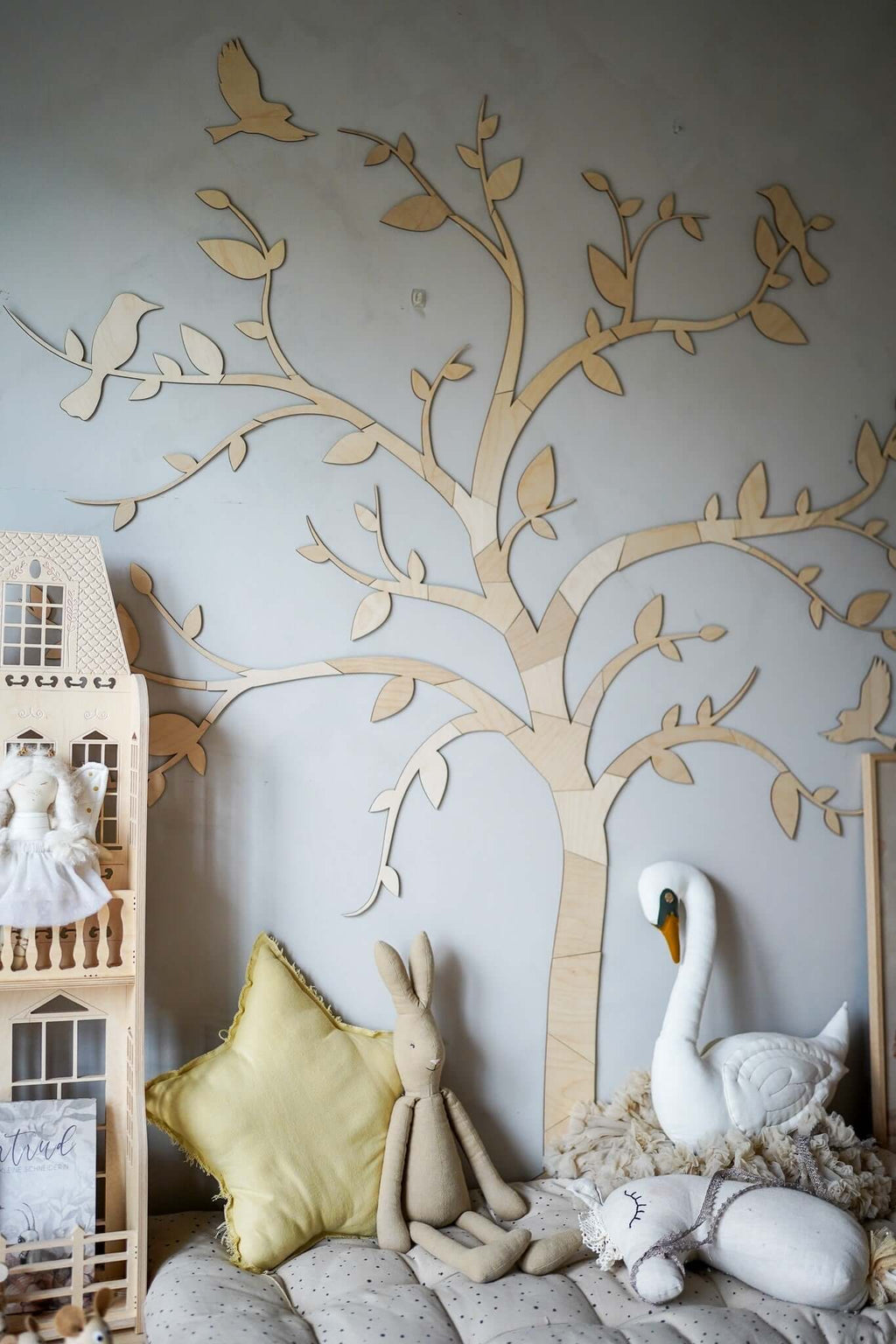 Wooden wall decoration tree birds on a nursery wall with plush toys and decor in a cozy setting.